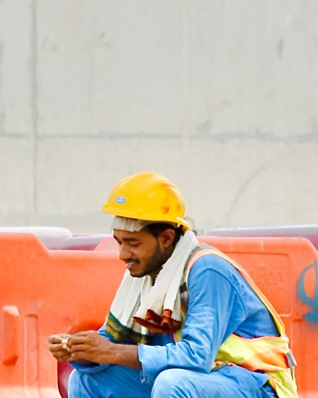A worker on a break sitting on a bucket, looking at his phone