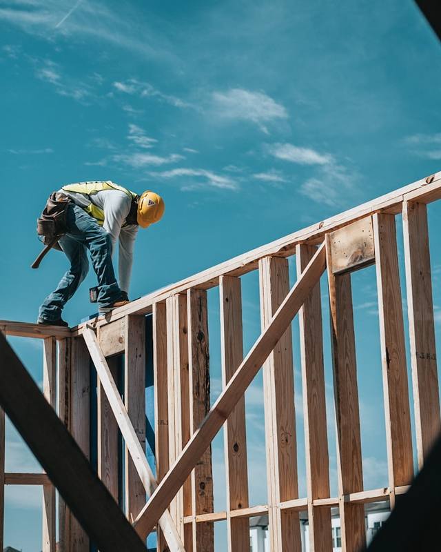 A framer working on a house frame against a blue sky