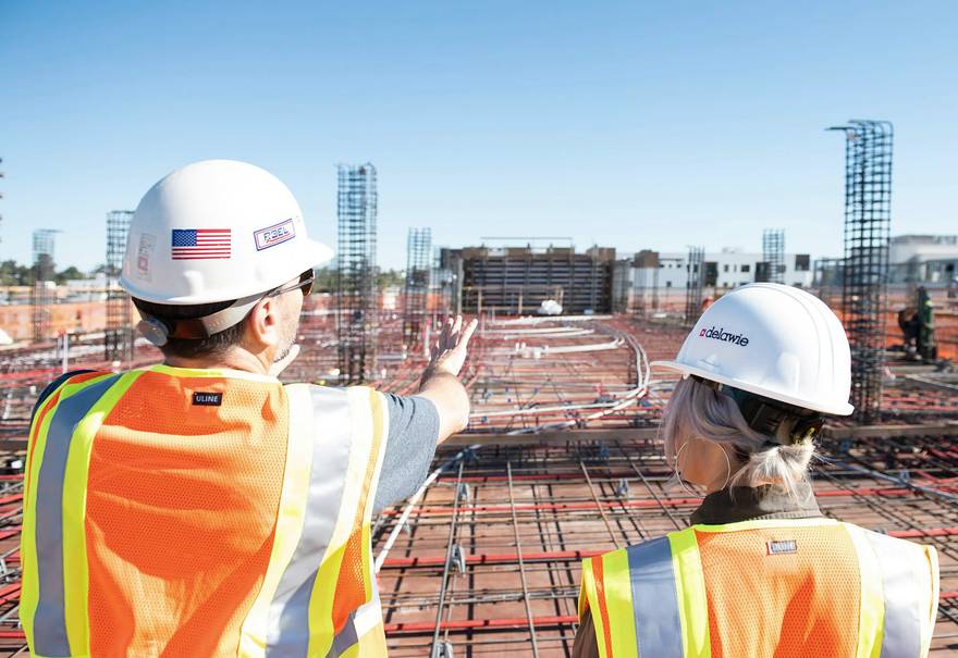 Two workers in safety vests on a jobsite, one pointing something out to the other