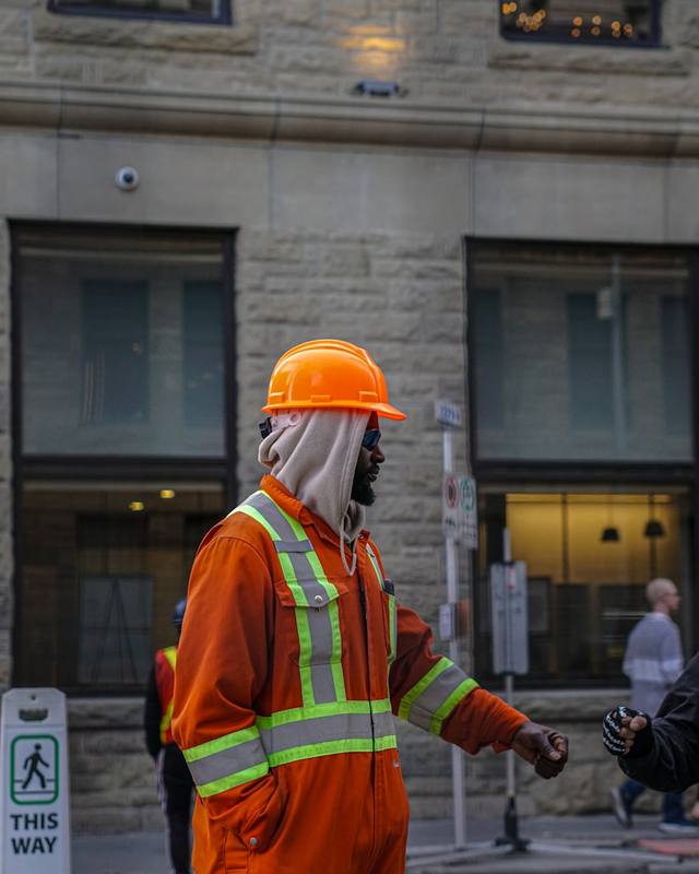 A worker in orange coveralls and a hard hat on a city street